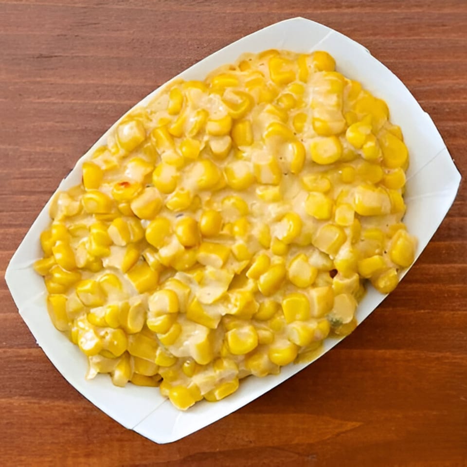 Creamed corn in a white paper tray, a classic side dish from Smokin' Jones BBQ.