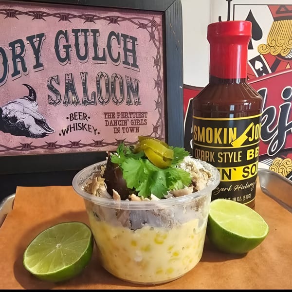 Smokin' Jones BBQ sauce bottle next to a cup of elote with limes and a saloon sign.
