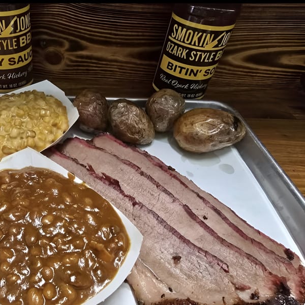 Smokin' Jones BBQ brisket, baked beans, creamed corn, and potatoes with BBQ sauce bottles.
