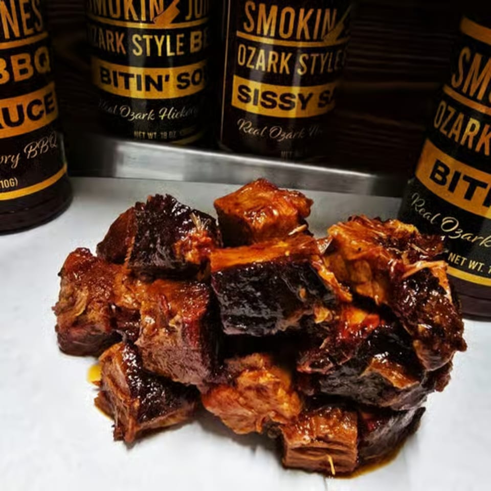 Smokin' Jones BBQ burnt ends with bottles of Ozark-style BBQ sauce in the background.