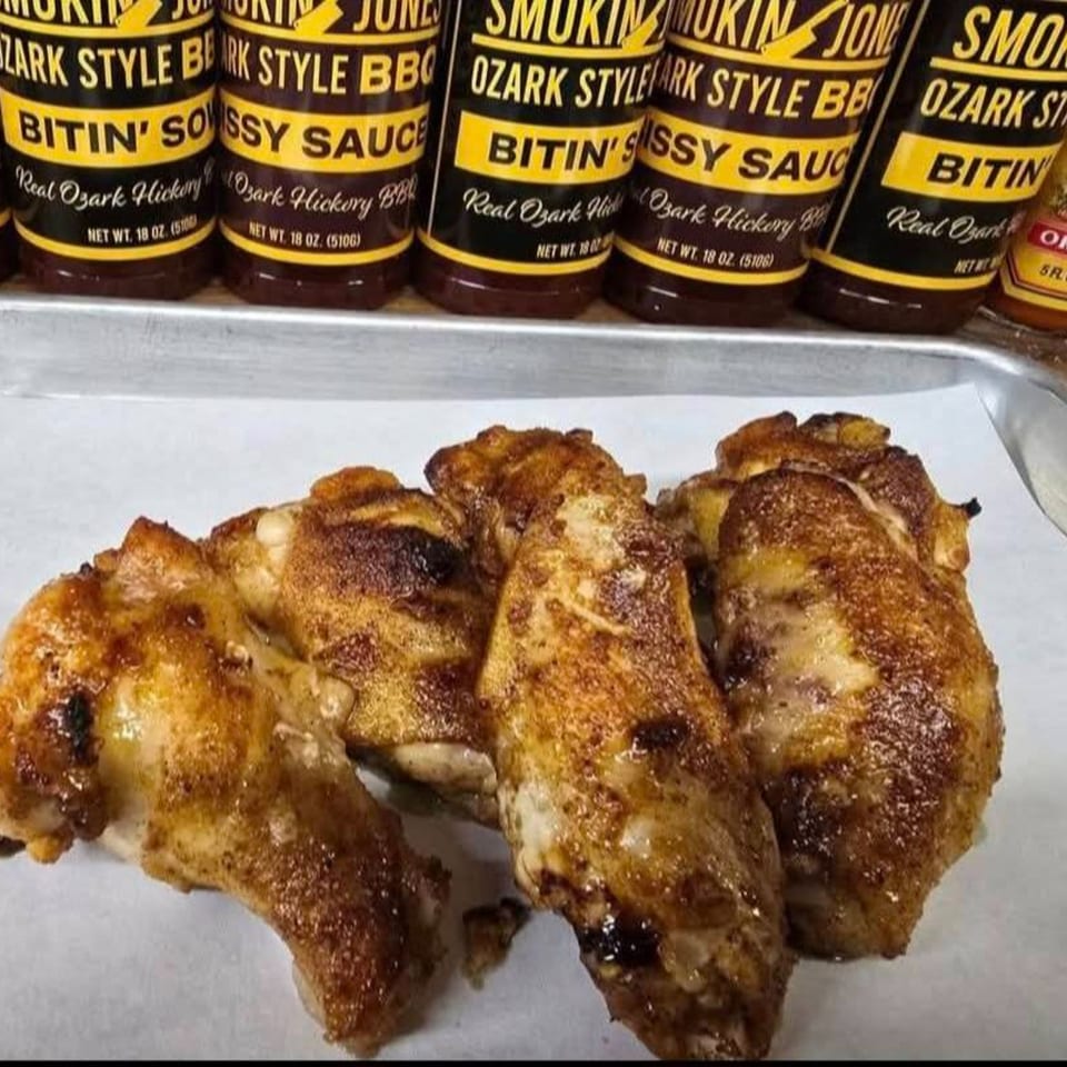 Smoked chicken wings on a tray with bottles of Smokin' Jones Ozark Style BBQ sauce in the background.