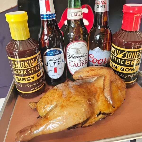 A whole smoked chicken on a tray, surrounded by Smokin' Jones BBQ sauces and beer bottles.